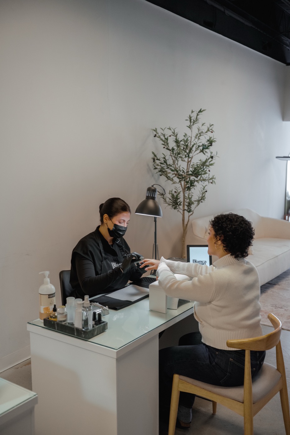 Inside Blanca Beauty Bar, a manicurist working on a client at the manicure station, olive tree behind, soft daylight